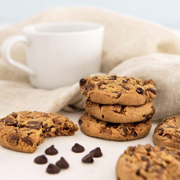 A plate of freshly baked banana bread cookies with golden edges, showcasing their soft and chewy texture, surrounded by ripe bananas and a glass of milk.
