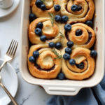 A baking dish filled with unbaked blueberry cheesecake rolls, showing swirls of creamy filling and fresh blueberries, ready to be baked